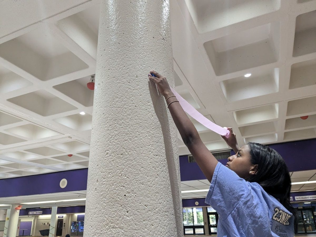 Sophomore Winta Solomon hangs up streamers after school on Oct. 15 in the commons. Solomon was one of the many students who planned and executed the homecoming commons decorations.