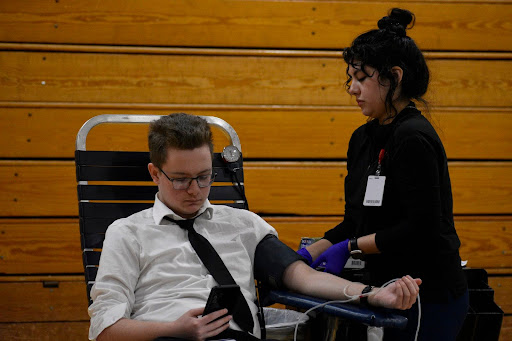 Junior Preston Brueckmann donates blood while on his phone for ImpactLife at Parkway North High School on Feb. 28. The process of drawing takes about 8-10 minutes but they have donors wait before going back to class to monitor them for any side effects.